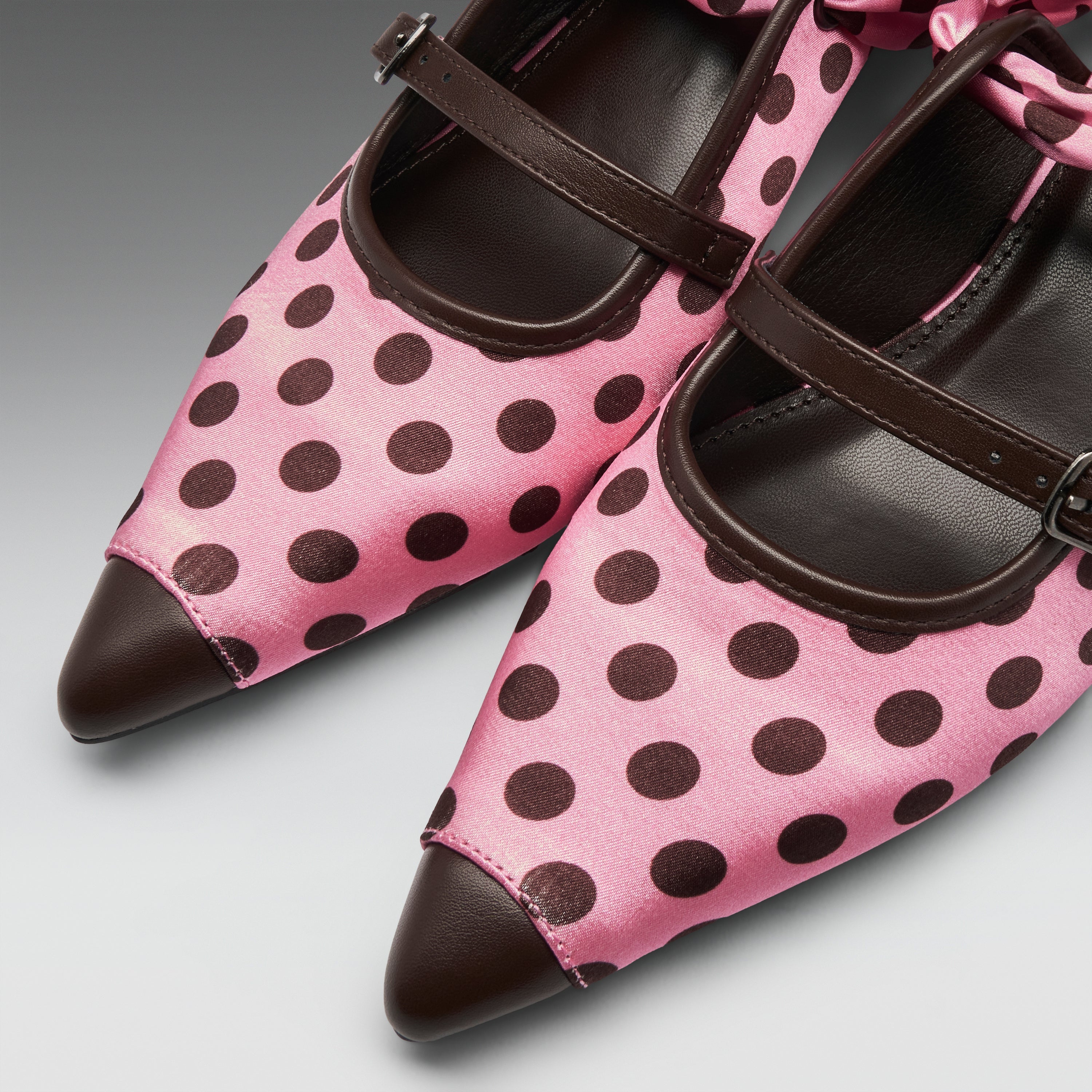 Pink satin Mary Jane shoes with dark brown polka dots, dark brown leather pointed toes, and matching dark brown straps, shown on a neutral gray background.