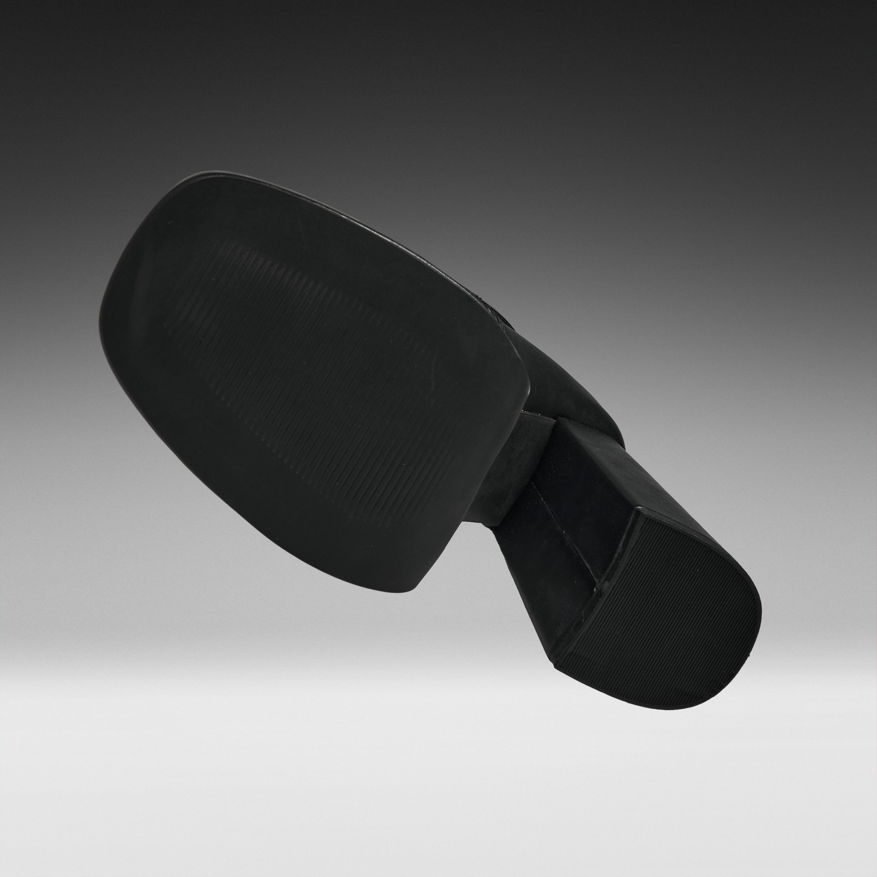 A black molded plastic component, likely a footrest or ergonomic support pad, shown floating against a dark-to-light gray gradient studio background.
