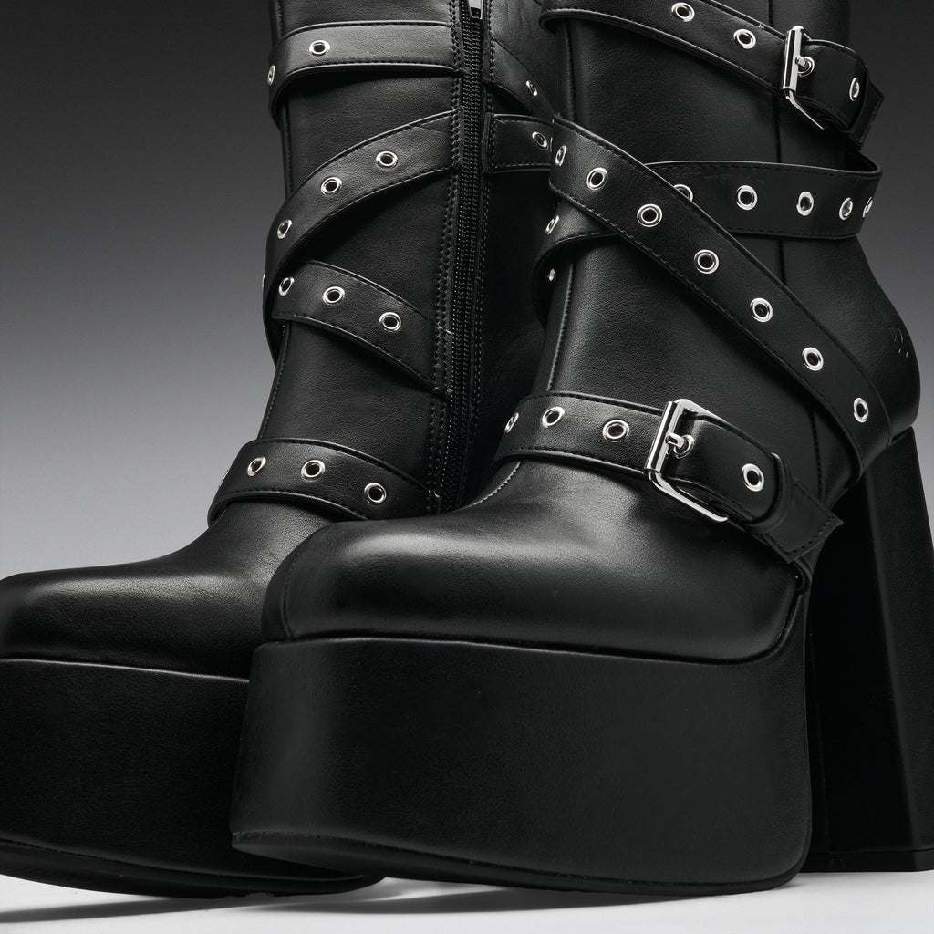Black leather platform ankle boots with multiple wraparound straps, silver-tone eyelets, and chunky block heels, shown in a studio close-up.