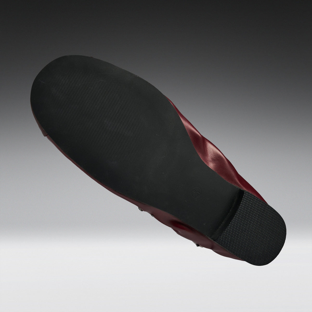 A single shoe shown from a high-angle back view, displaying a black textured outsole and a dark burgundy-red inner lining against a gray gradient background.