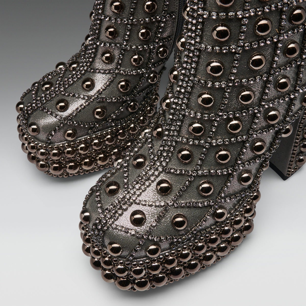 A pair of metallic dark gray platform ankle boots heavily embellished with rows of round bronze studs and rhinestone-lined grommets, shown against a neutral gray background.