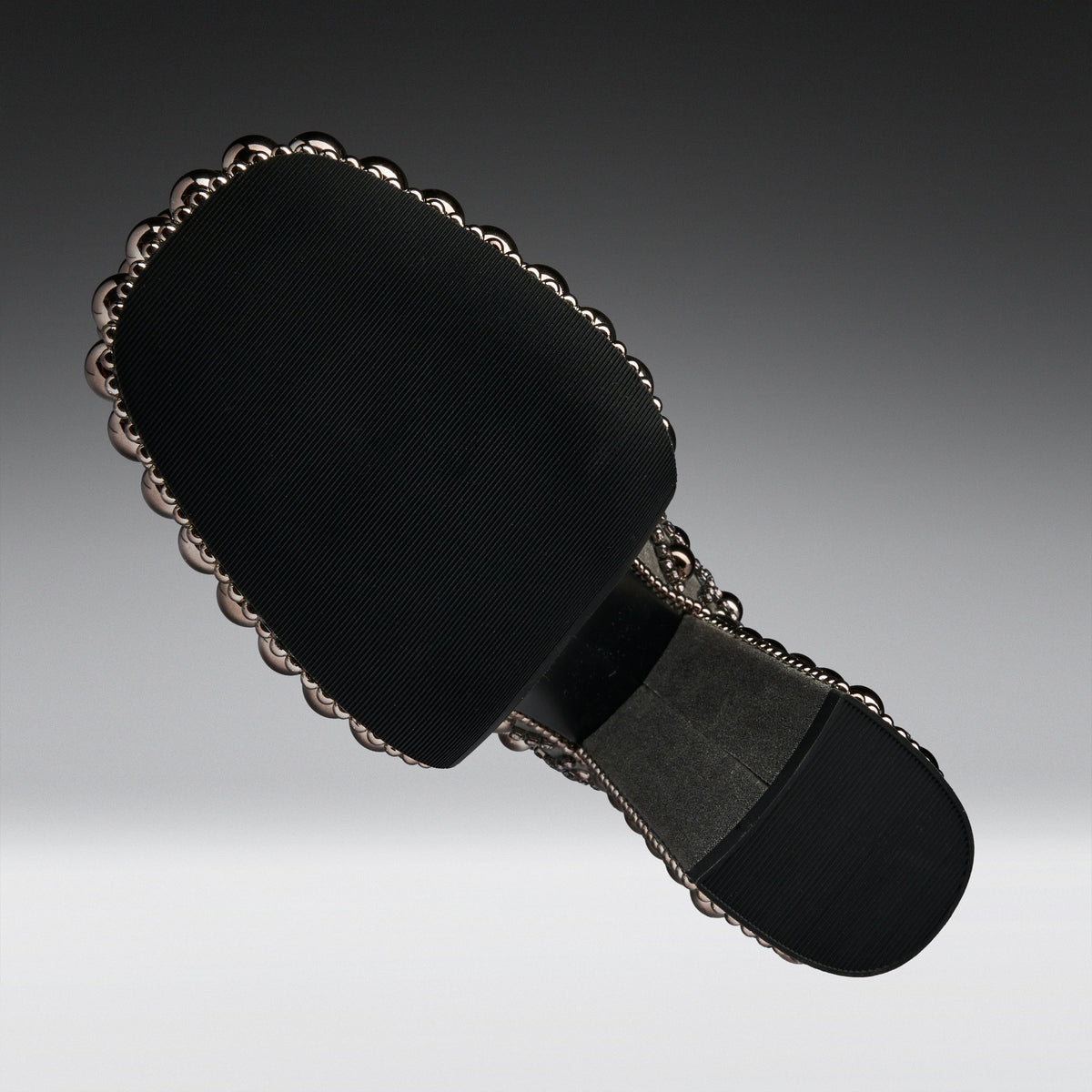 A black fabric-covered shoe sole with a decorative scalloped metallic edge and a dark gray cushioned section, shown on a gradient gray background.