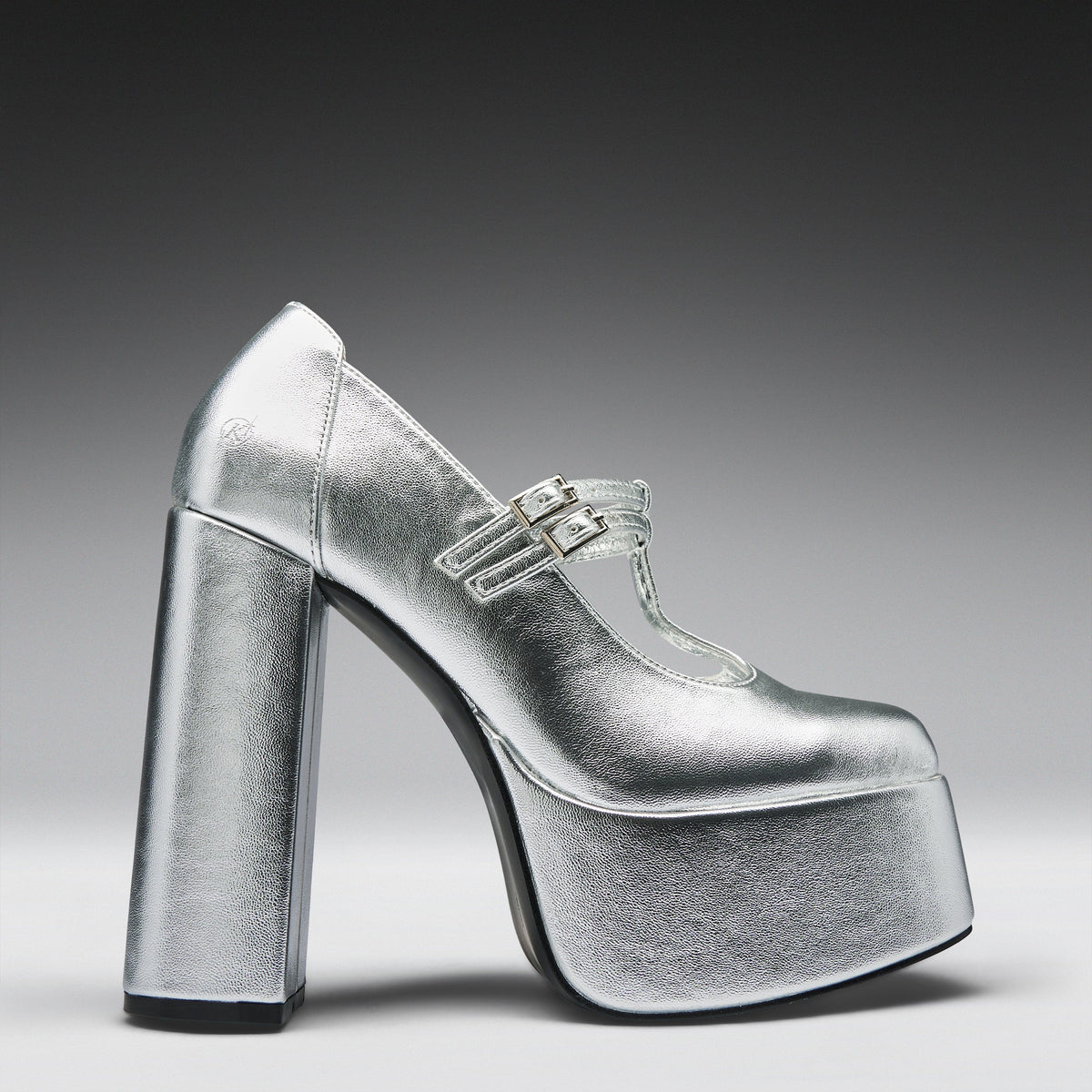 A metallic silver platform high-heeled shoe with a Mary Jane strap and double buckle detail, shown from a side profile on a dark-to-light gray gradient background.