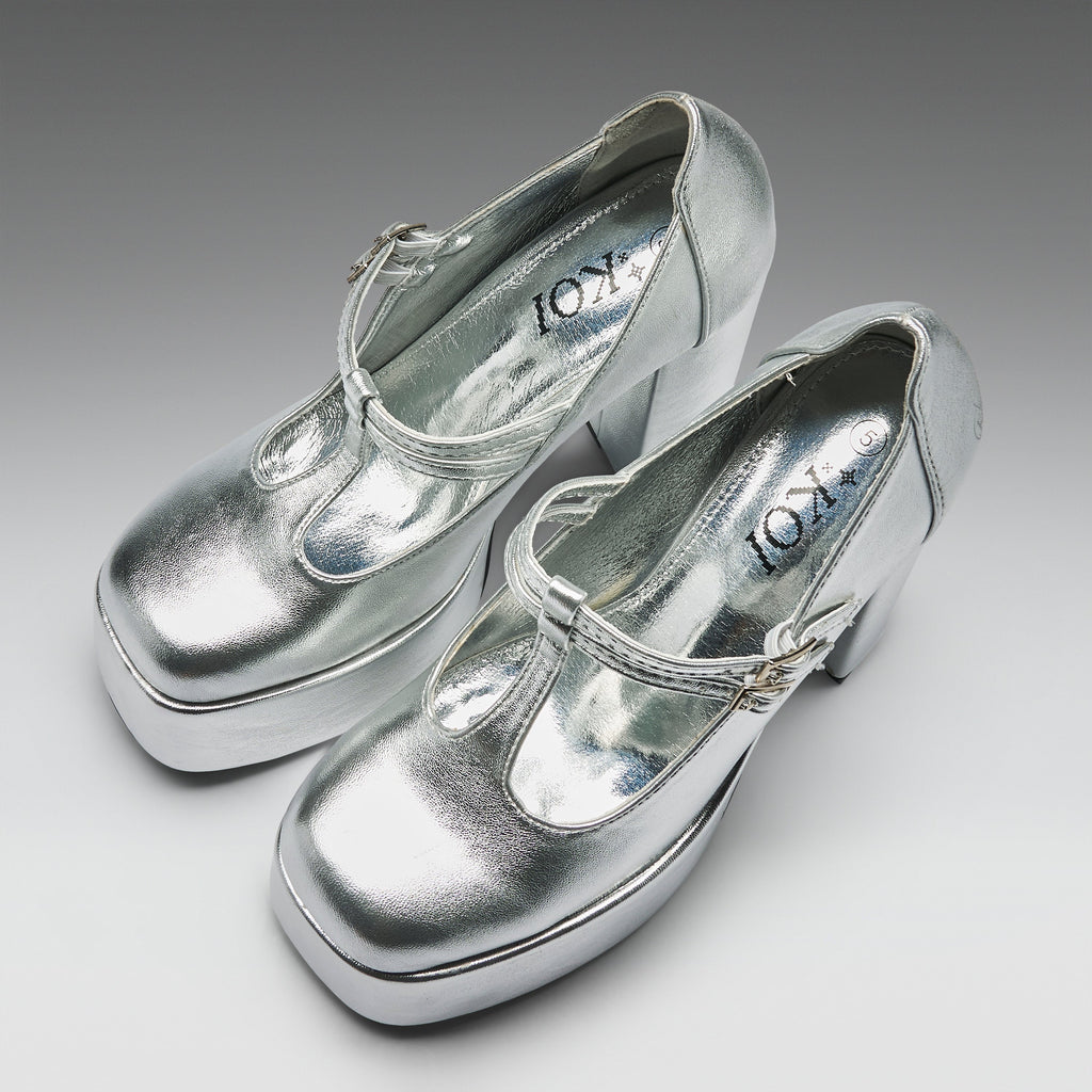A pair of metallic silver Mary Jane platform heels with block heels and buckle straps, displayed on a neutral gray gradient background. The brand name 'KOT' is visible on the insoles.