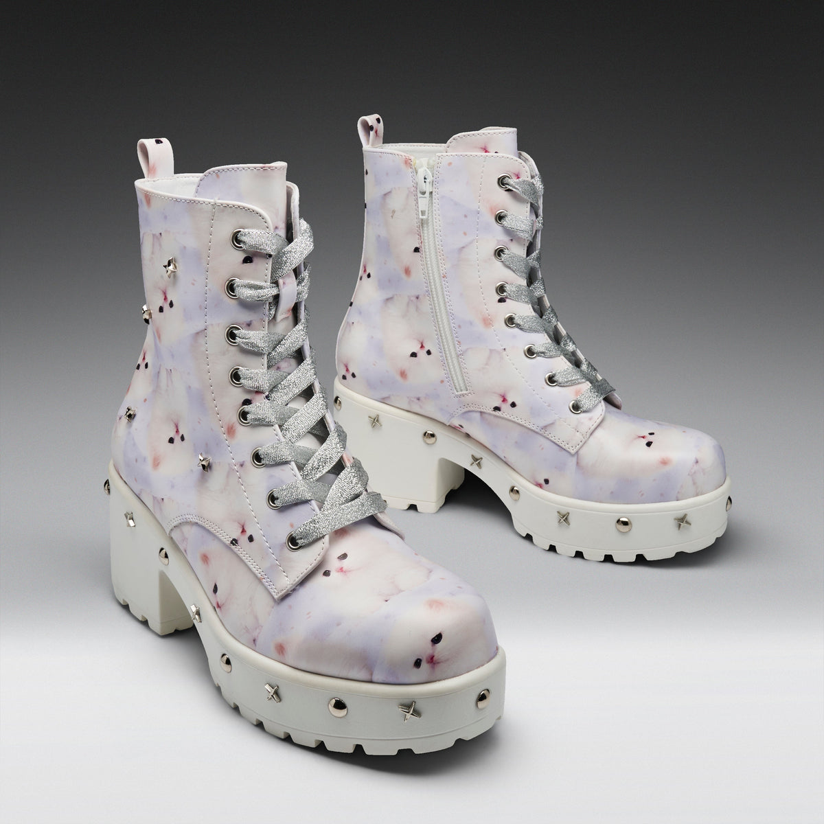 A pair of chunky lace-up ankle boots with a white base and a pastel purple, pink, and blue watercolor-style floral pattern. The boots feature silver metal studs on the thick white lug soles, gray laces, and a side zipper.