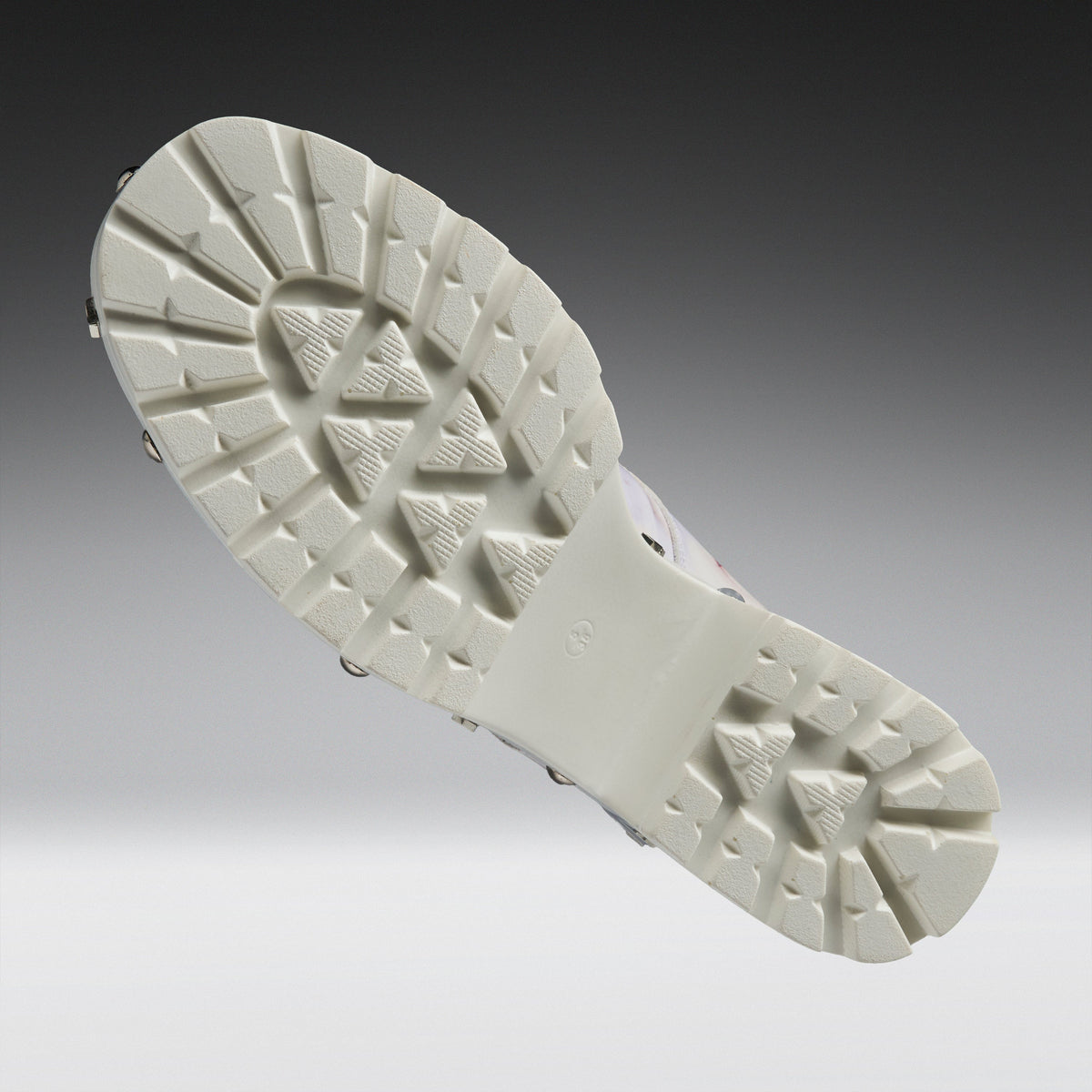 The outsole of a white athletic shoe, showing its textured tread pattern and metal cleats, photographed against a dark-to-light gray gradient studio background.
