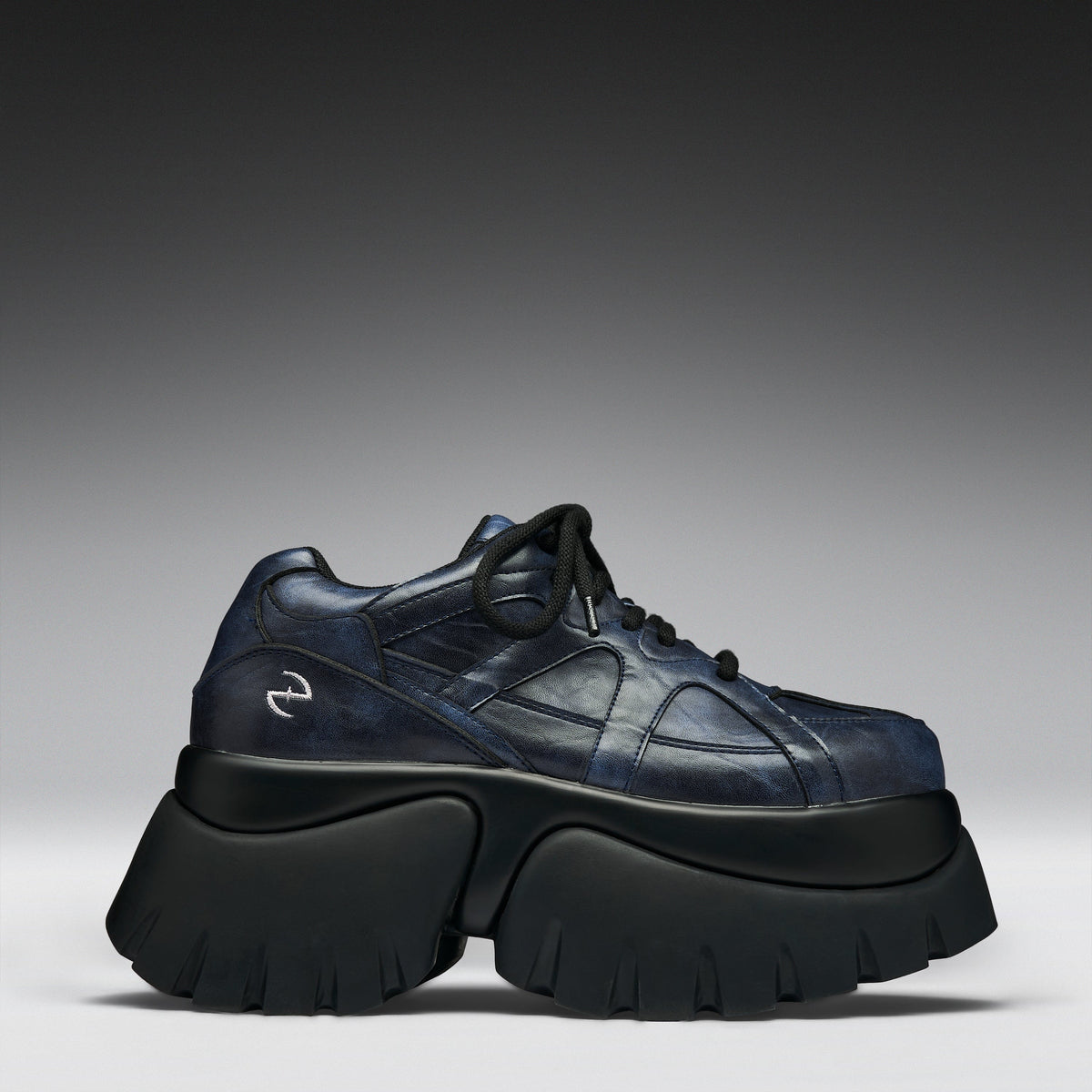 A single dark navy blue leather sneaker with a chunky black platform sole, photographed from a side profile against a gray gradient studio background.
