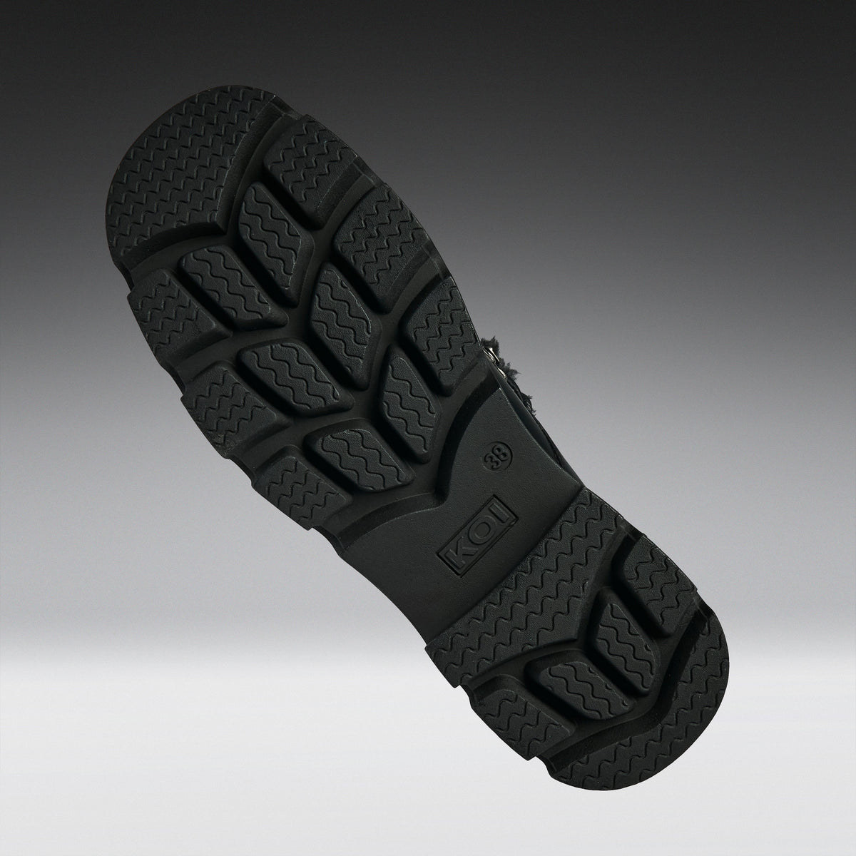 A close-up of a black textured shoe sole, showing the tread pattern and embossed K-Swiss logo, set against a dark gray gradient background.