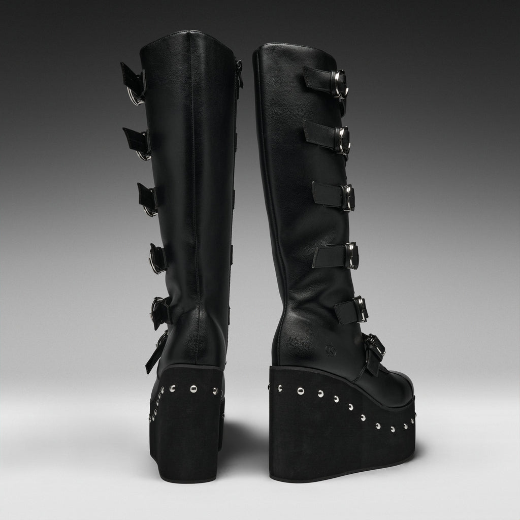 A pair of black knee-high platform boots with multiple buckle straps down the side, shown from the back against a dark gray gradient studio background.