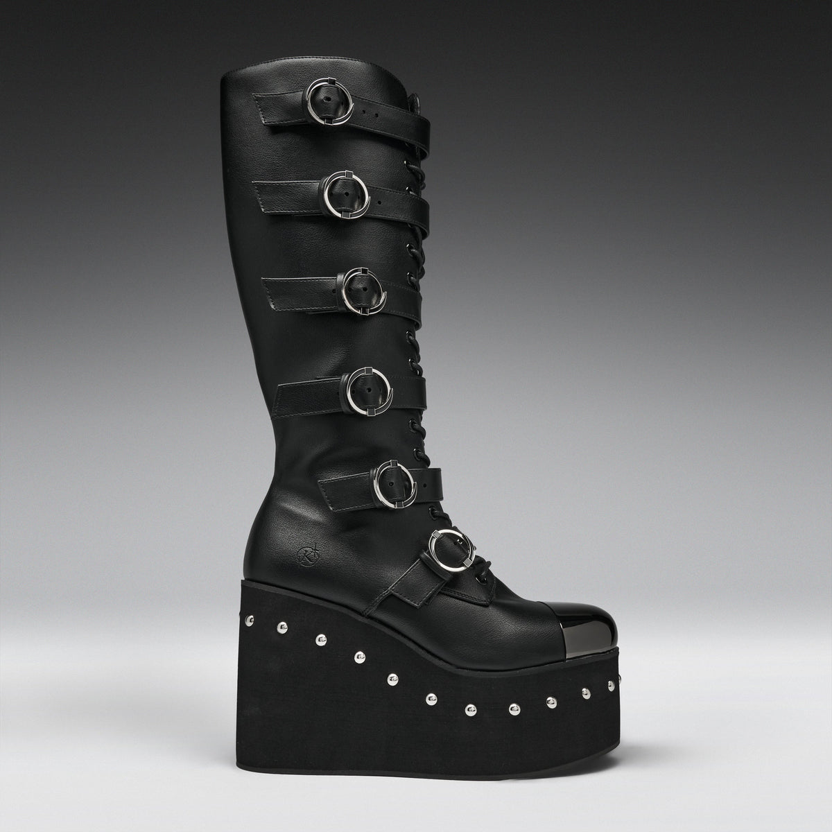 A tall black leather platform boot with multiple horizontal strap details and silver-tone circular buckles, photographed against a dark gray gradient studio background.
