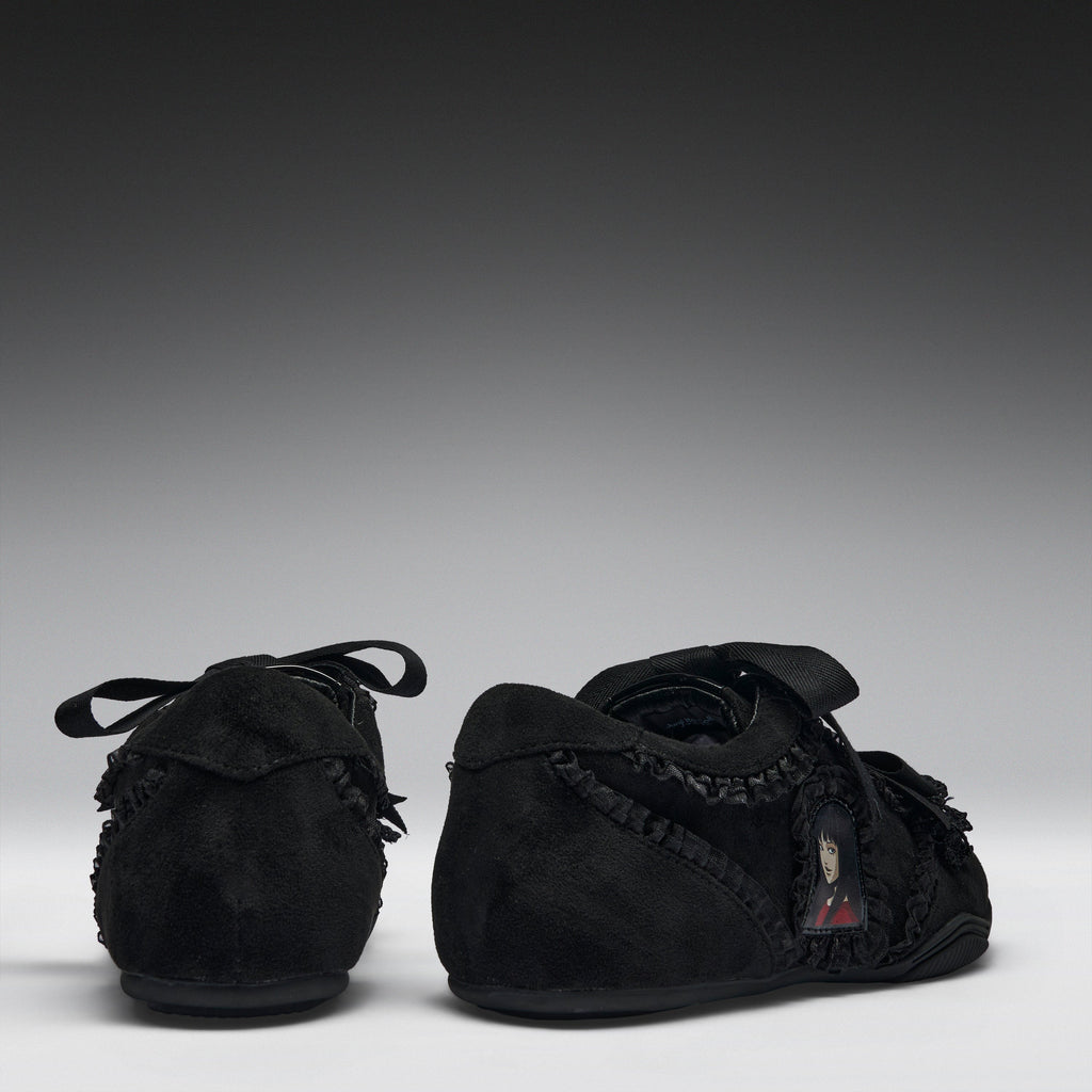 A pair of black suede baby moccasins with fringed trim and lace-up front details, shown from the back and side against a dark gray gradient background.