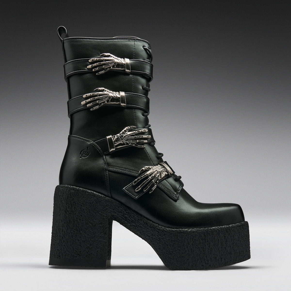 A black leather ankle boot with a chunky platform sole and high block heel, decorated with three silver metallic skeleton hand embellishments on the straps, shown against a dark gray gradient background.