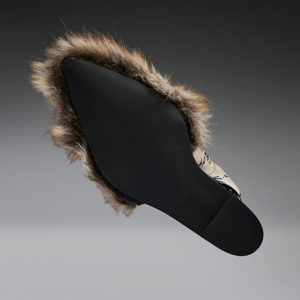 A black slip-on shoe with a brown and beige faux-fur trim, shown from a side profile against a dark gray gradient background.
