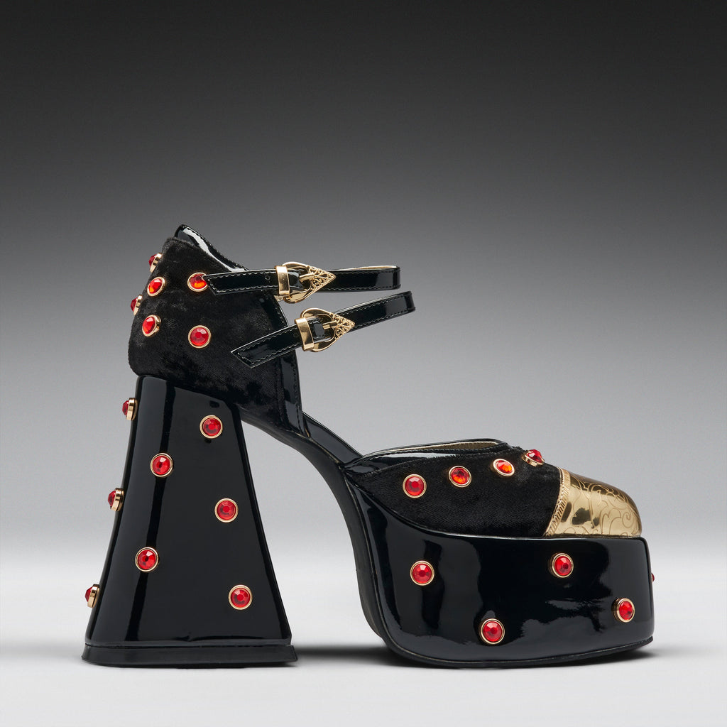 A single black patent leather platform sandal with a chunky block heel, embellished with red rhinestones and gold-tone hardware, shown against a dark gray gradient background.