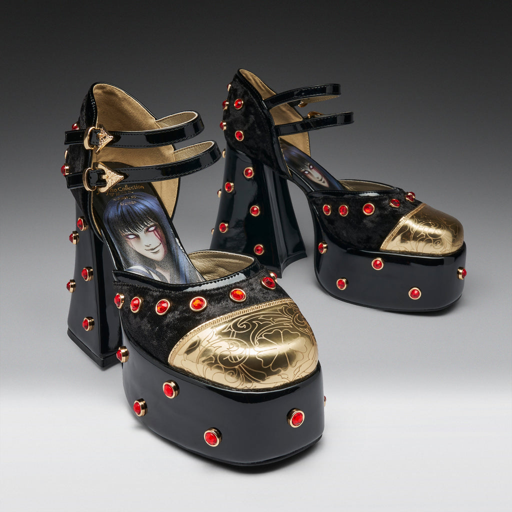 A pair of black platform high heels with gold metallic toe caps, red rhinestone studs, and double ankle straps. The insole of the front shoe features a printed illustration of an anime character.