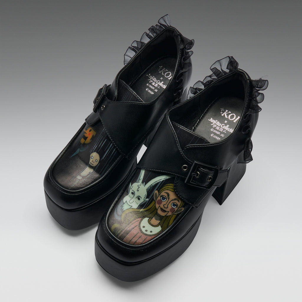 A pair of black platform Mary Jane-style shoes with ruffled trim and block heels, featuring printed character artwork on the toe boxes. The shoes are photographed on a clean light gray studio background.