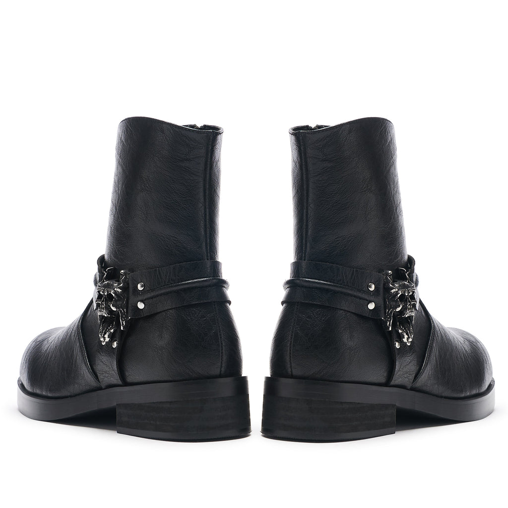 A pair of vintage black leather biker boots with stacked hardware and a decorative element on the heel.