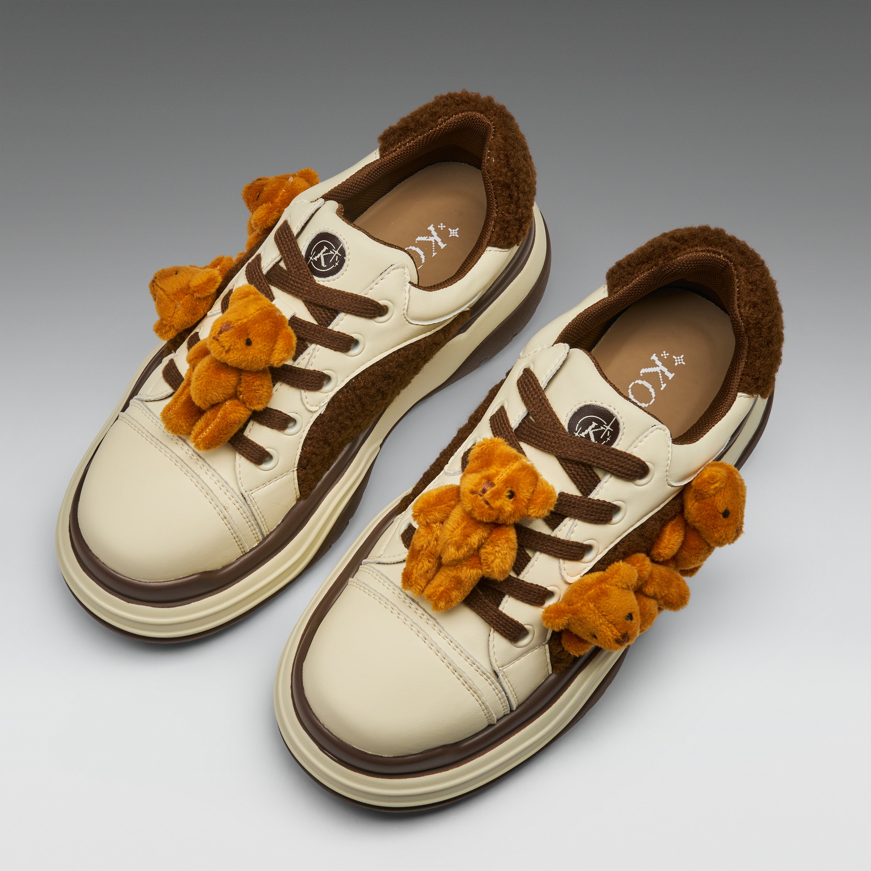 Pair of cream sneakers with brown accents and small teddy bears on a gradient background