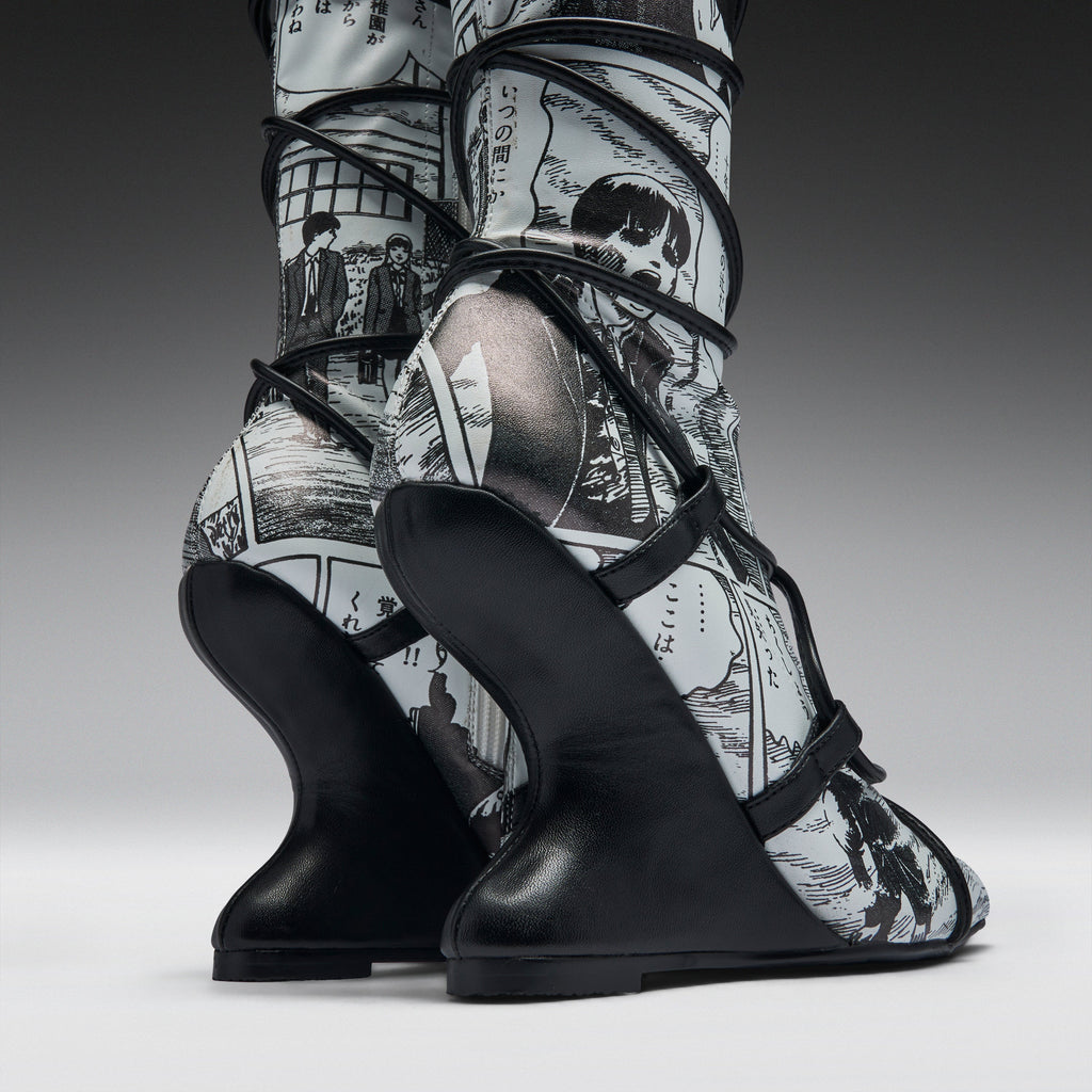 A pair of high-heeled boots with sculptural black wedge heels and black straps, featuring a black-and-white manga comic book print on the uppers, shown against a dark gray studio background.