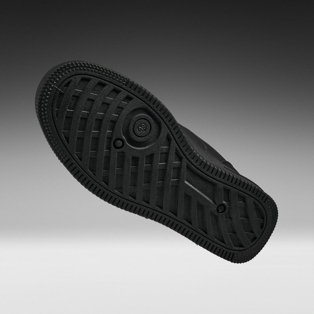 A black rubber shoe sole shown from a top-down angle against a dark gray to light gray gradient background.