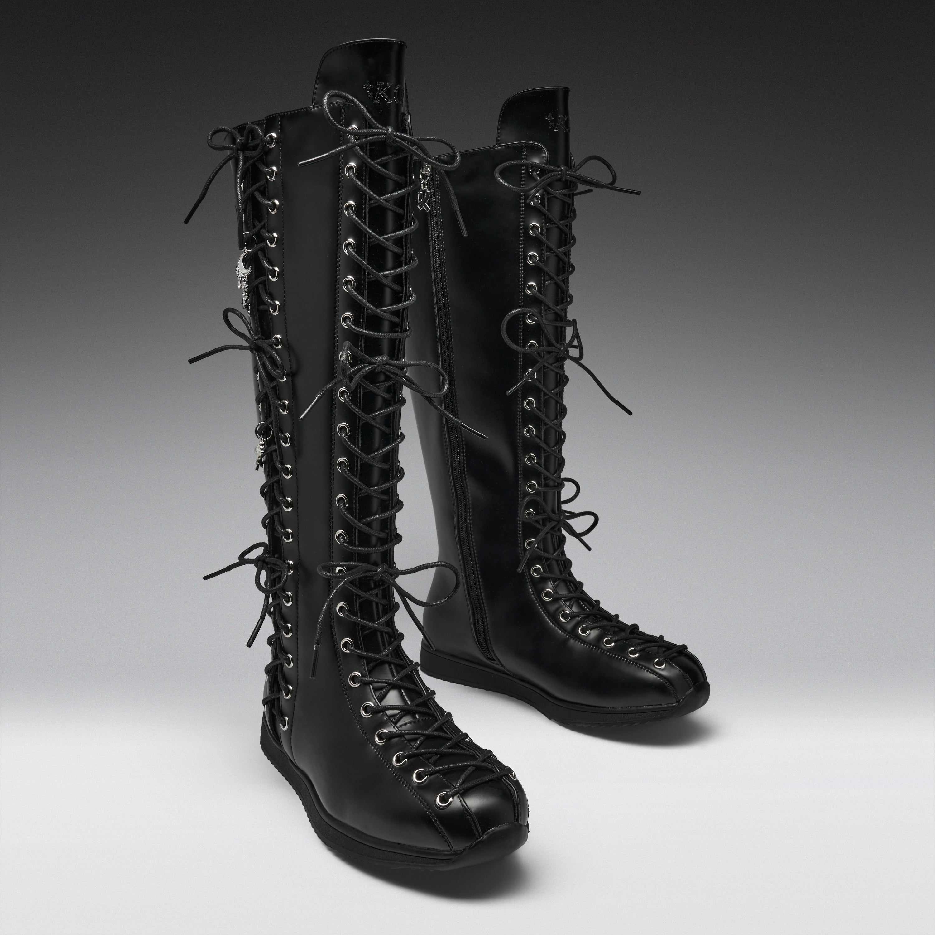 A pair of black leather knee-high lace-up boots with multiple decorative laces and silver-tone eyelets, photographed on a clean gray studio background.