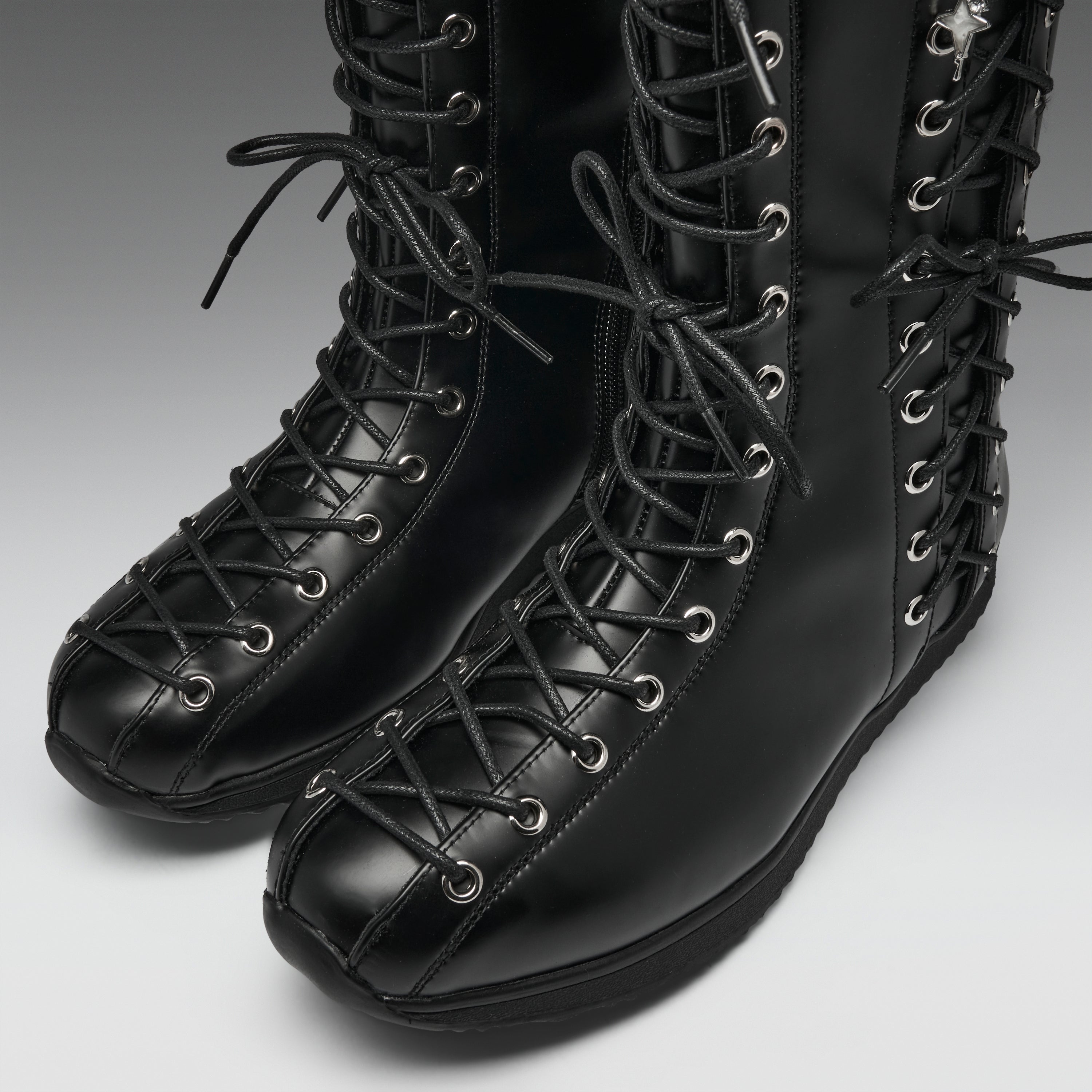 A pair of black leather lace-up boots with silver metal eyelets, shown on a neutral gray background.