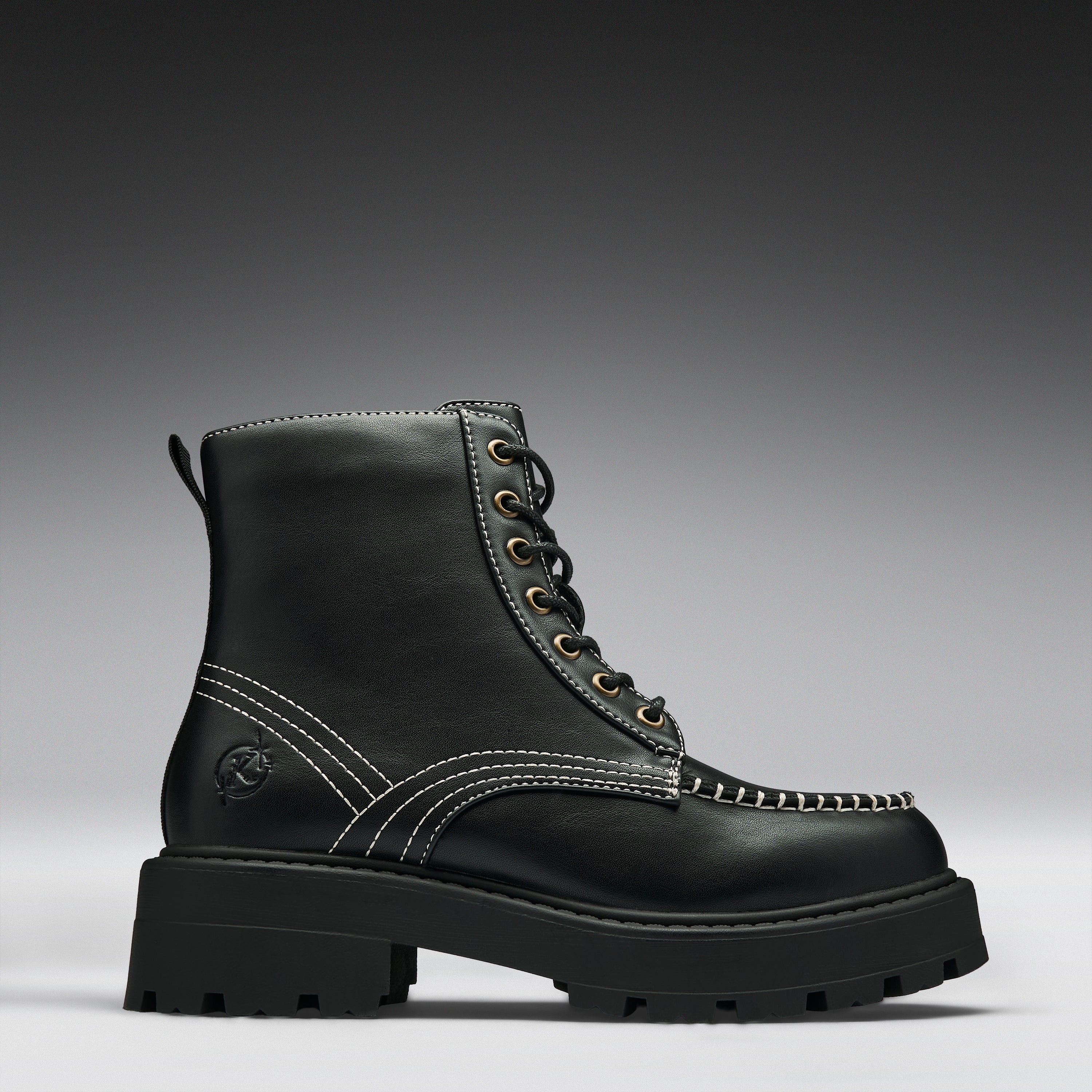 A single black leather lace-up boot with contrast white stitching, gold-tone eyelets, and a chunky lug sole, photographed on a dark-to-light gray gradient studio background.