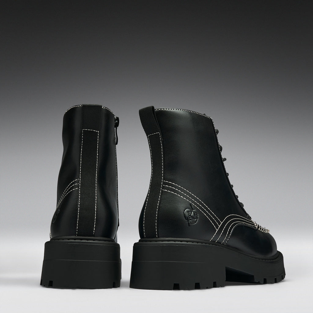 A pair of black leather lace-up ankle boots with chunky lug soles, shown from the back and side against a dark gray gradient background.
