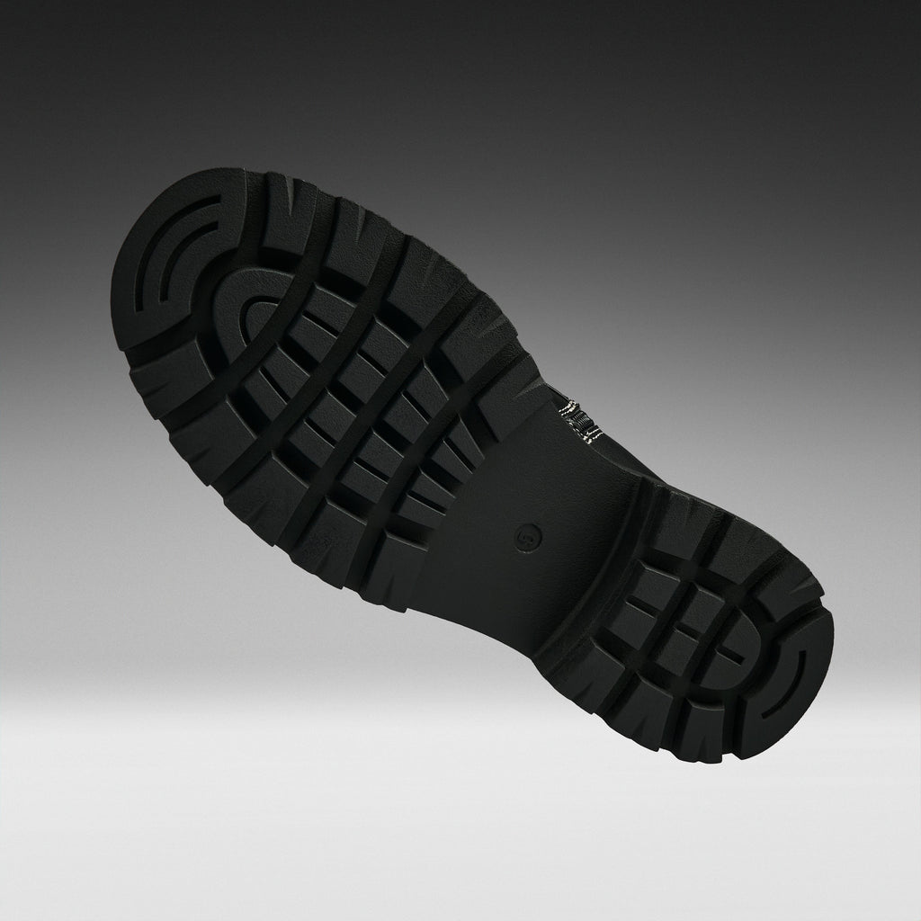 A close-up of a black rubber shoe sole with deep tread patterns, shown floating against a dark-to-light gray gradient background.