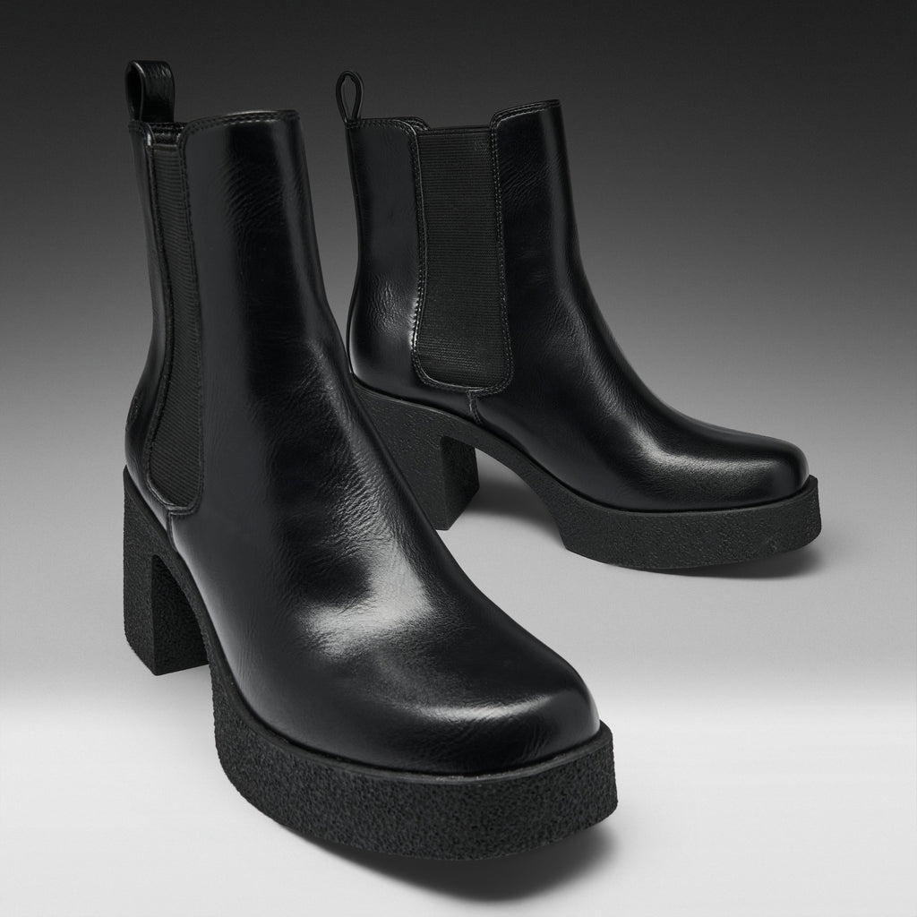 A pair of black leather Chelsea-style ankle boots with platform soles and block heels, photographed on a clean gray studio background.