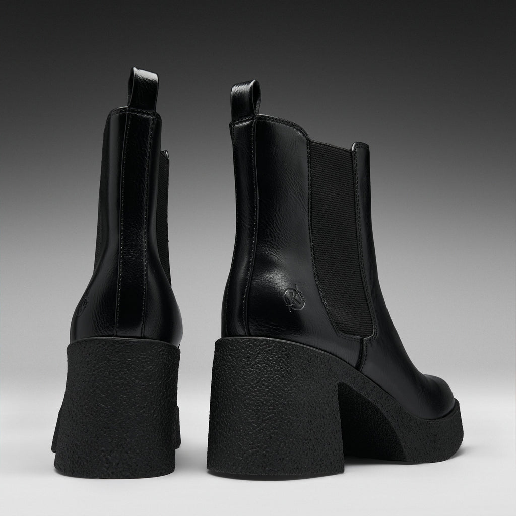 A pair of black leather Chelsea-style ankle boots with chunky block heels, shown from the back and side against a dark gray gradient studio background.