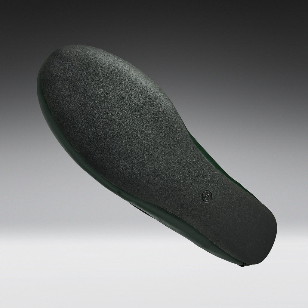 A single shoe sole shown floating against a dark-to-light gray gradient background. The sole is dark charcoal gray with a subtle green tint along the inner edge.
