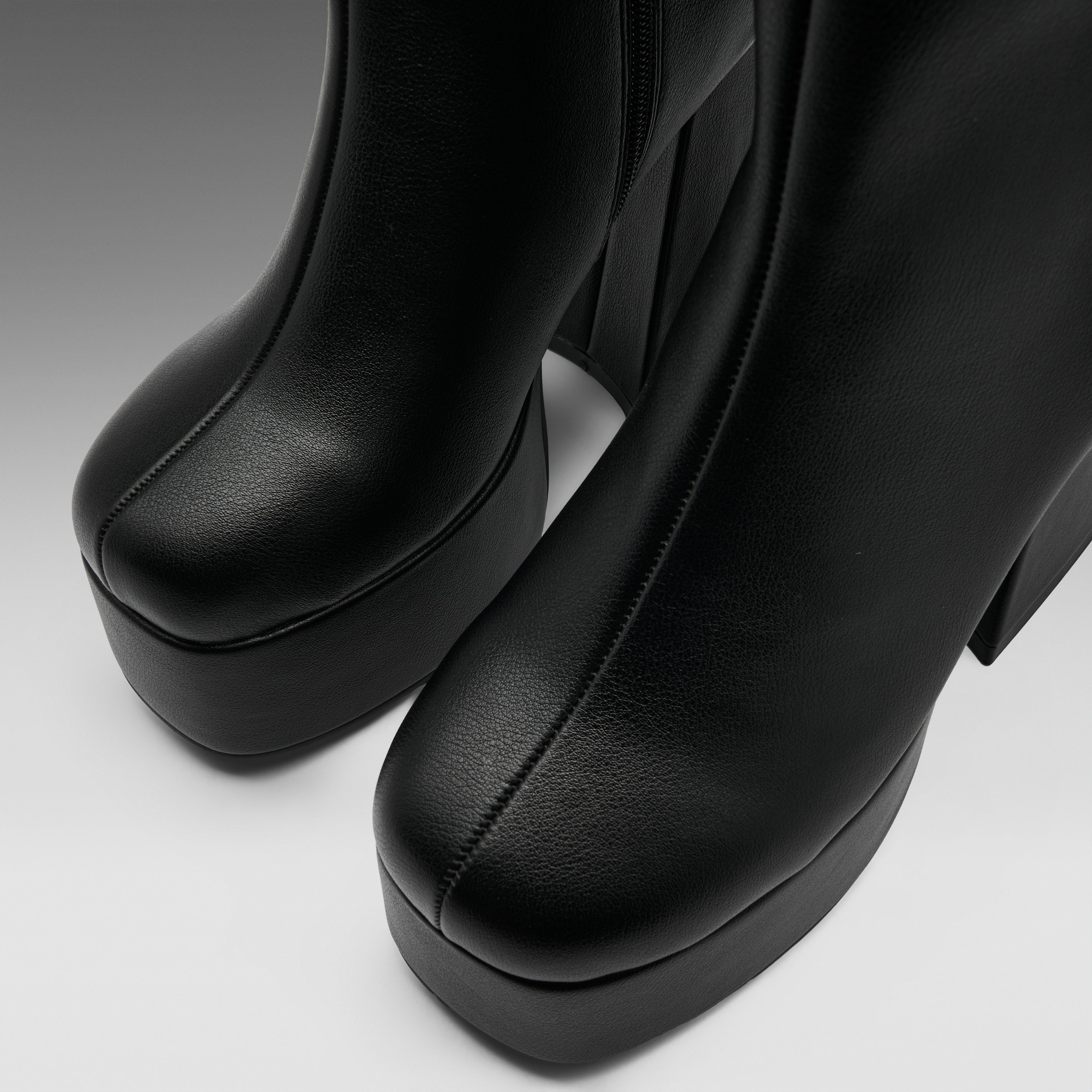 Close-up of a pair of black leather platform ankle boots with a chunky block heel, showing the toe and side profile against a neutral gray background.
