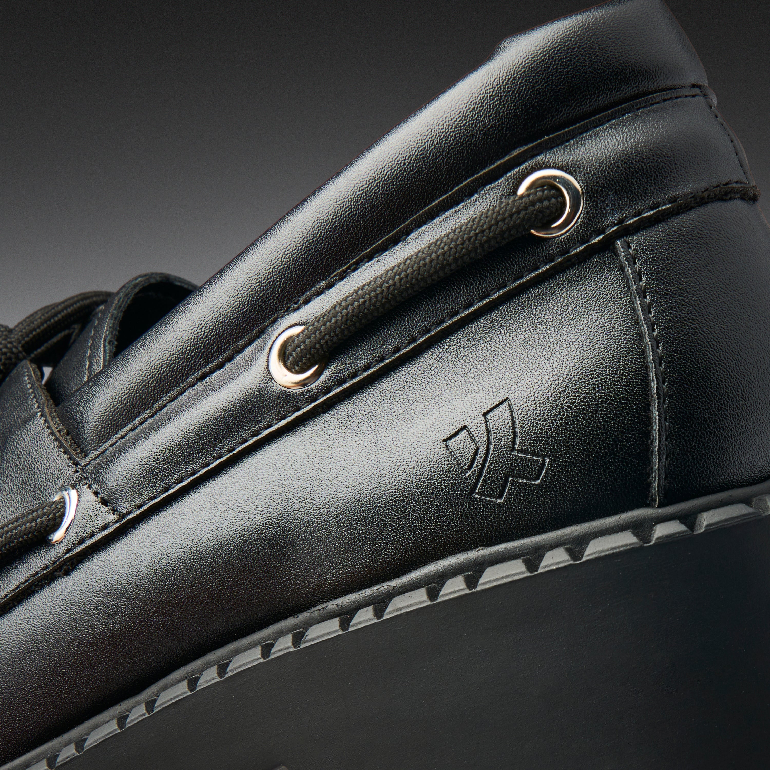 Close-up of a black leather shoe with a brand logo on a dark background