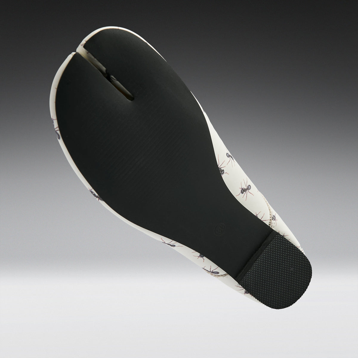 A split-foot flat sandal shown from the sole view, featuring a black textured midfoot and heel with a white and black ant-patterned outsole, set against a dark-to-light gray gradient background.