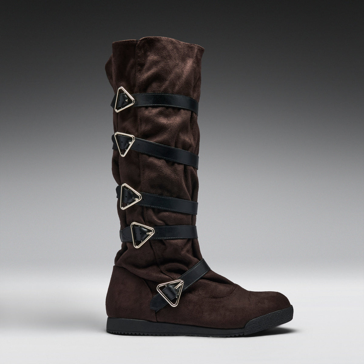 A dark brown suede knee-high boot with multiple black straps and silver-tone triangular metal hardware, shown in profile against a gray gradient studio background.