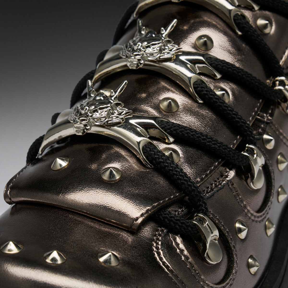 Close-up of a metallic dark brown leather sneaker with black laces, silver studs, and ornate silver metal eyelets.