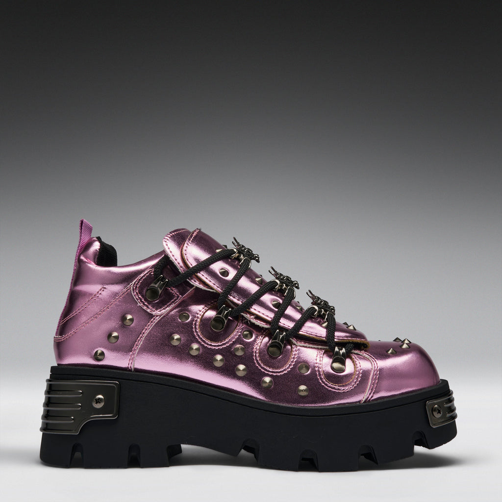 A metallic pink platform sneaker with black laces, silver studs, and a chunky black sole, shown from a side profile on a gray gradient background.