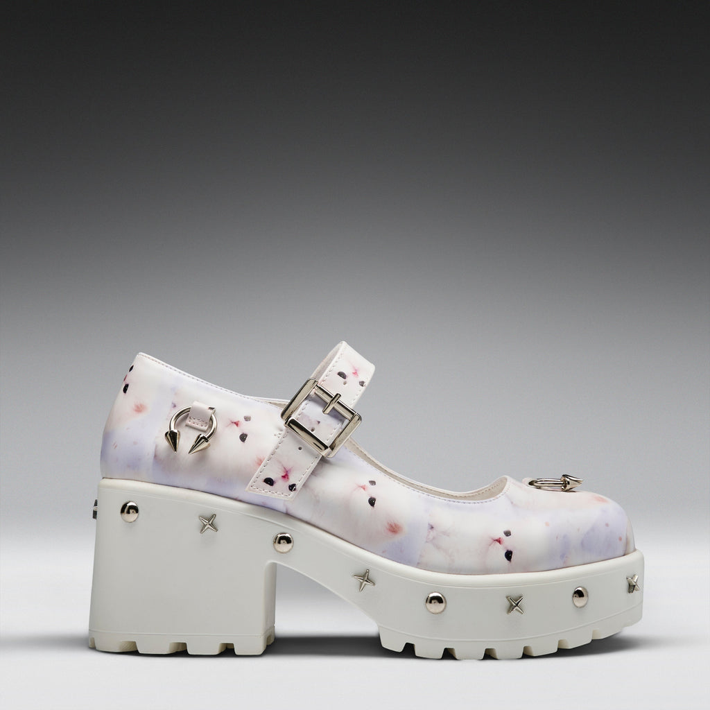 A white platform Mary Jane shoe with a subtle pastel watercolor pattern, silver-tone buckles, and decorative metal studs on a gray gradient background.