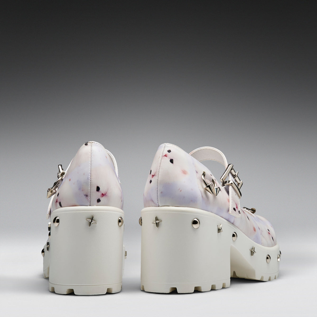 A pair of chunky platform Mary Jane shoes shown from the back, featuring a white base with a light purple and pink floral pattern, silver-tone metal studs, and buckle straps.