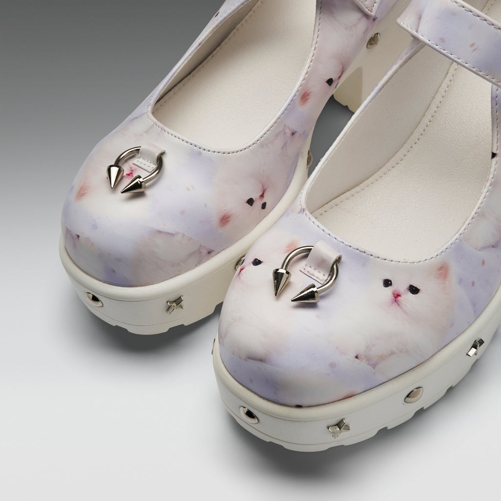 A pair of platform Mary Jane shoes featuring a pastel white and lavender cat print, decorated with silver metal hoop rings on the toes and small metallic studs on the soles.