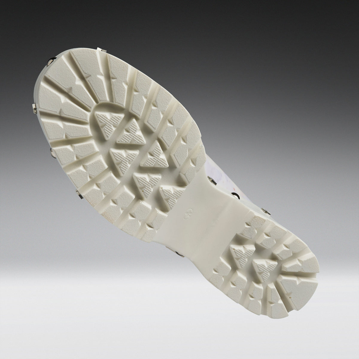 A close-up studio shot of a white athletic shoe sole, showing the textured tread pattern and small metal spikes on the outsole, set against a dark-to-light gray gradient background.