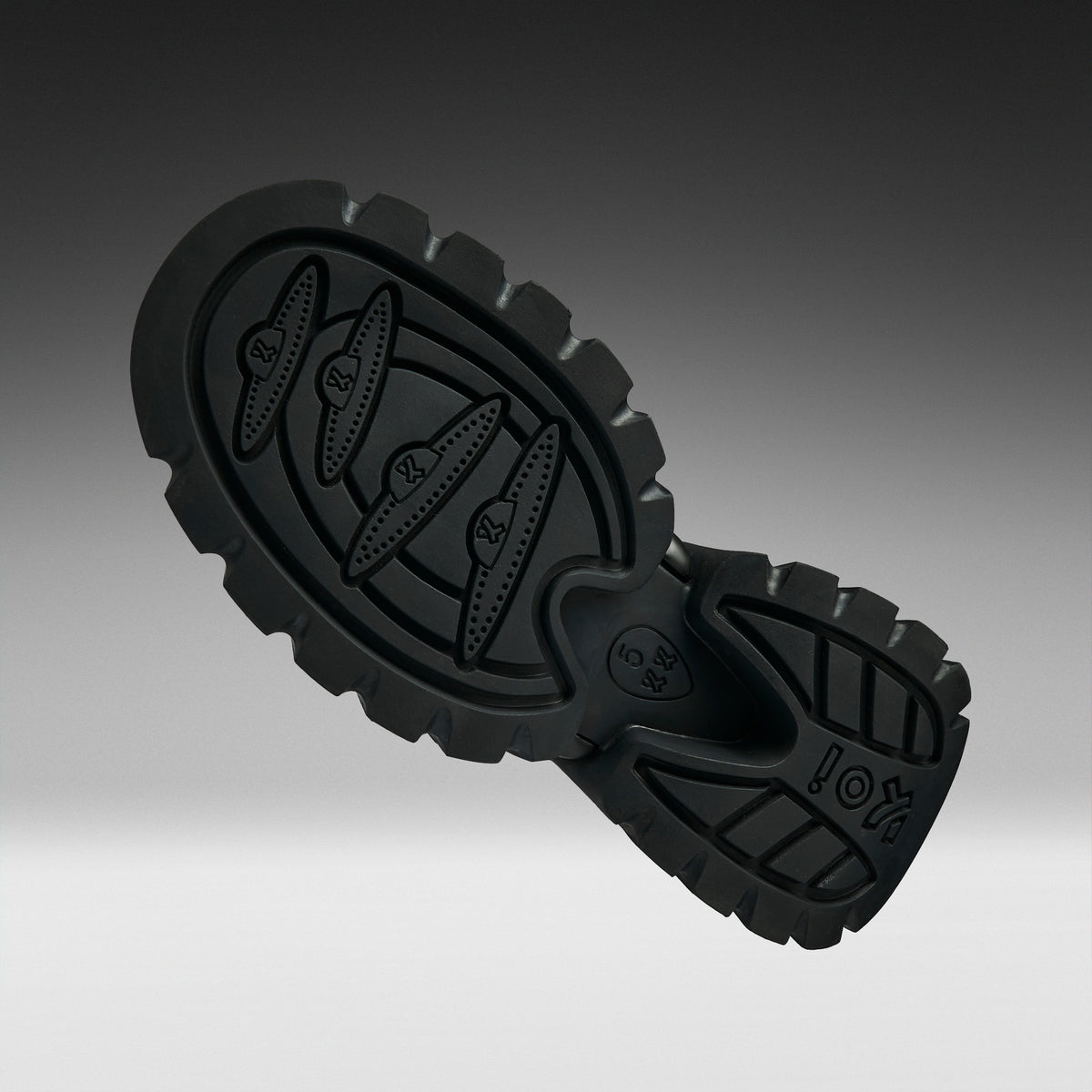 A close-up of a black rubber shoe sole with textured tread patterns and embossed branding, shown against a dark-to-light gray gradient background.