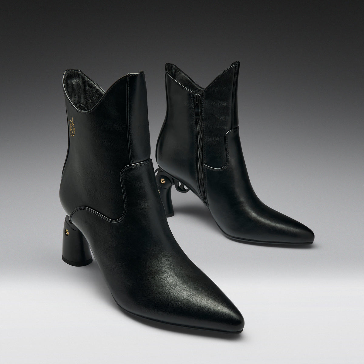 A pair of black leather ankle boots with pointed toes and block heels, displayed on a clean gray gradient studio background.